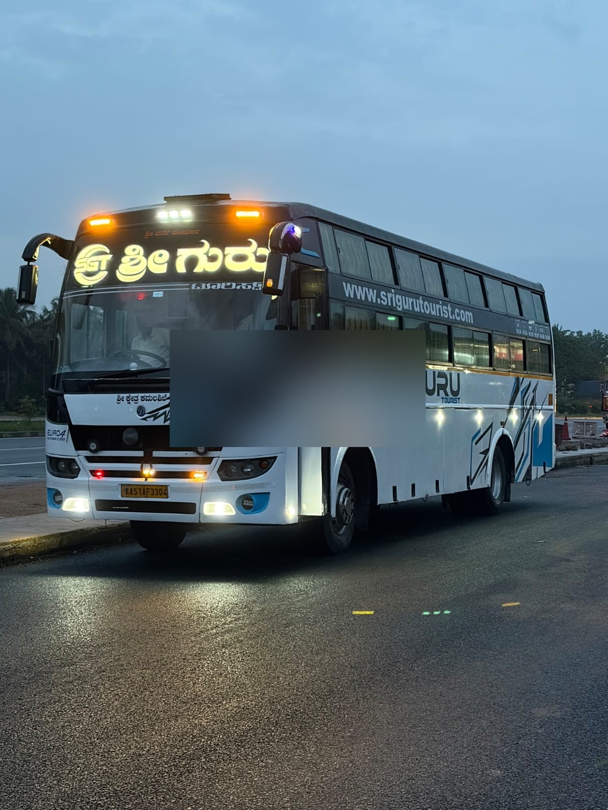 Sri Guru Tourist bus with lights on at dusk